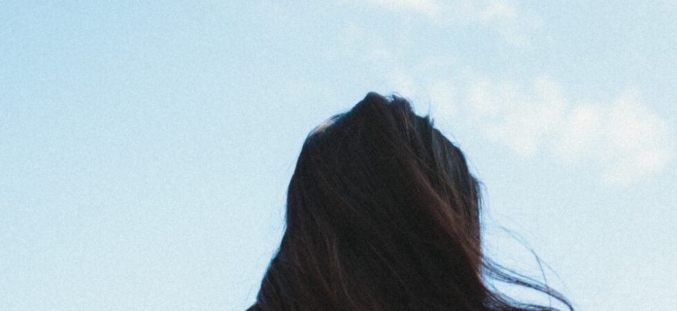 Woman with healthy shiny hair during monsoon season standing near a window with rainy weather outside